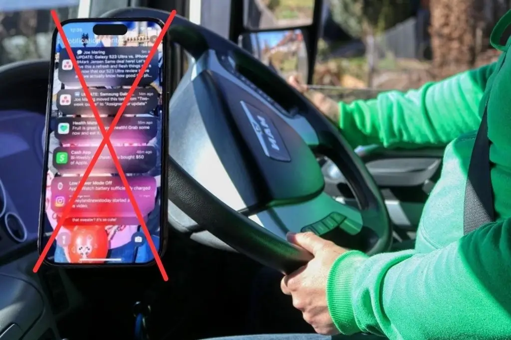 Lorry driver holding steering wheel next to a mobile phone showing incoming notifications