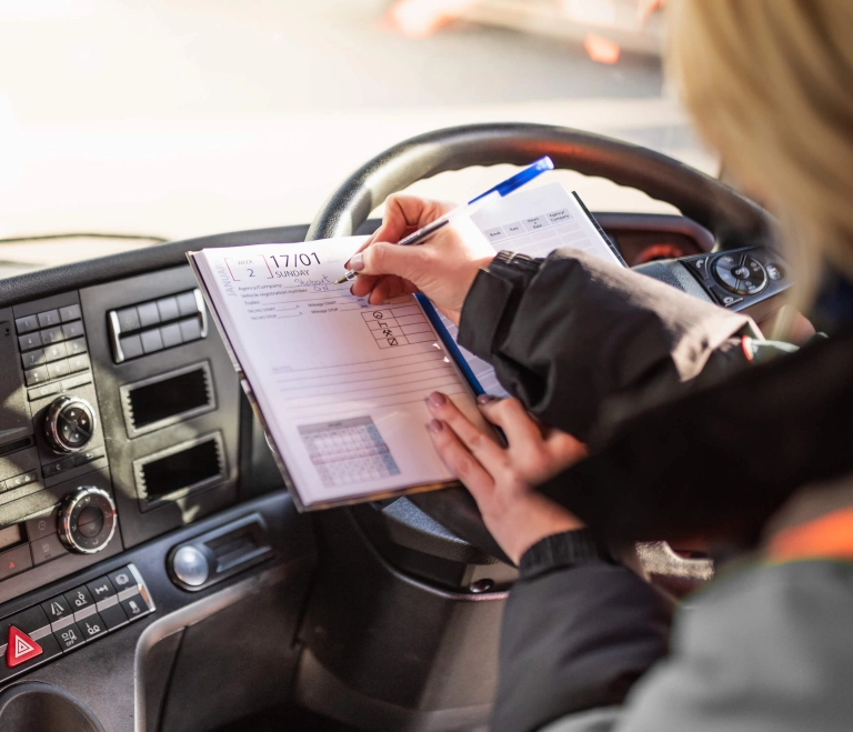 HGV truck driver writing daily log entry in driver diary inside lorry cab